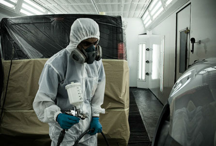 Technician in protective suit spray painting a vehicle in the booth